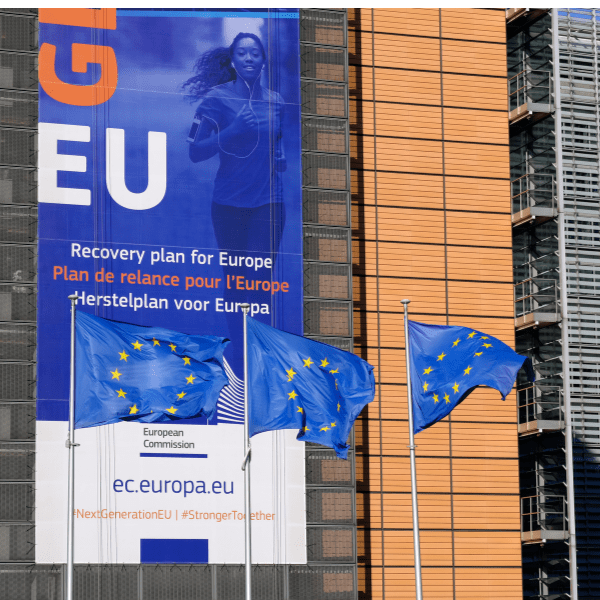 Three EU flags in front of a Eurozone recovery banner on the Berlaymont building of the European Commission